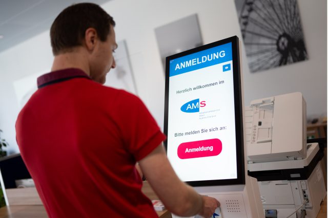 Ein Mann steht vor einem Bildschirm. Darauf ist "AMS. Anmeldung" zu lesen. Symbolbild für die Arbeitslosigkeit in Österreich.