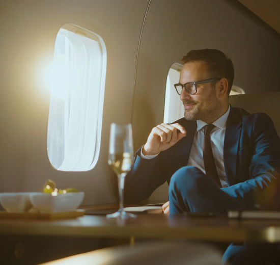Ein Mann in einem Privatjet trinkt Champagner und schaut aus dem Fenster. Symbolbild für eine Vermögensobergrenze.