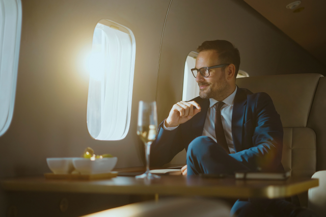 Ein Mann in einem Privatjet trinkt Champagner und schaut aus dem Fenster. Symbolbild für eine Vermögensobergrenze.