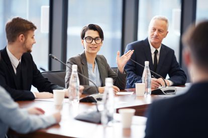 Porträt einer jungen Geschäftsfrau, die während einer Gruppendiskussion in einem Konferenzraum in ein Mikrofon spricht.